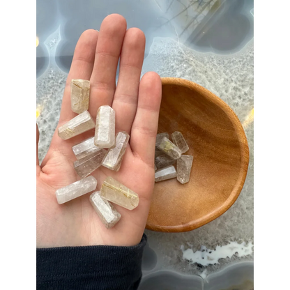 Hand holding clear faceted quartz crystal points with golden rutiles