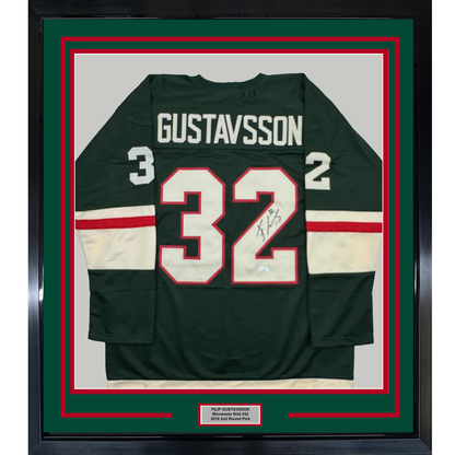 Framed dark green hockey jersey displaying number 32 with "GUSTAVSSON" nameplate and signature, bordered by red and white stripes, mounted in green and red matting with black frame.