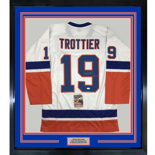 Framed white New York Islanders hockey jersey number 19 with "TROTTIER" nameplate, signed, displayed against blue and red matting with nameplate plaque.