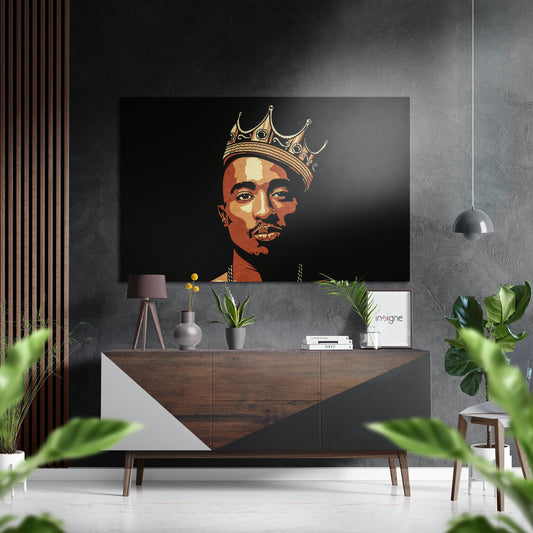Modern interior styling showing brushed aluminium wall art depicting a figure wearing a gold crown against black background, mounted above a wooden dresser with plants and accessories.