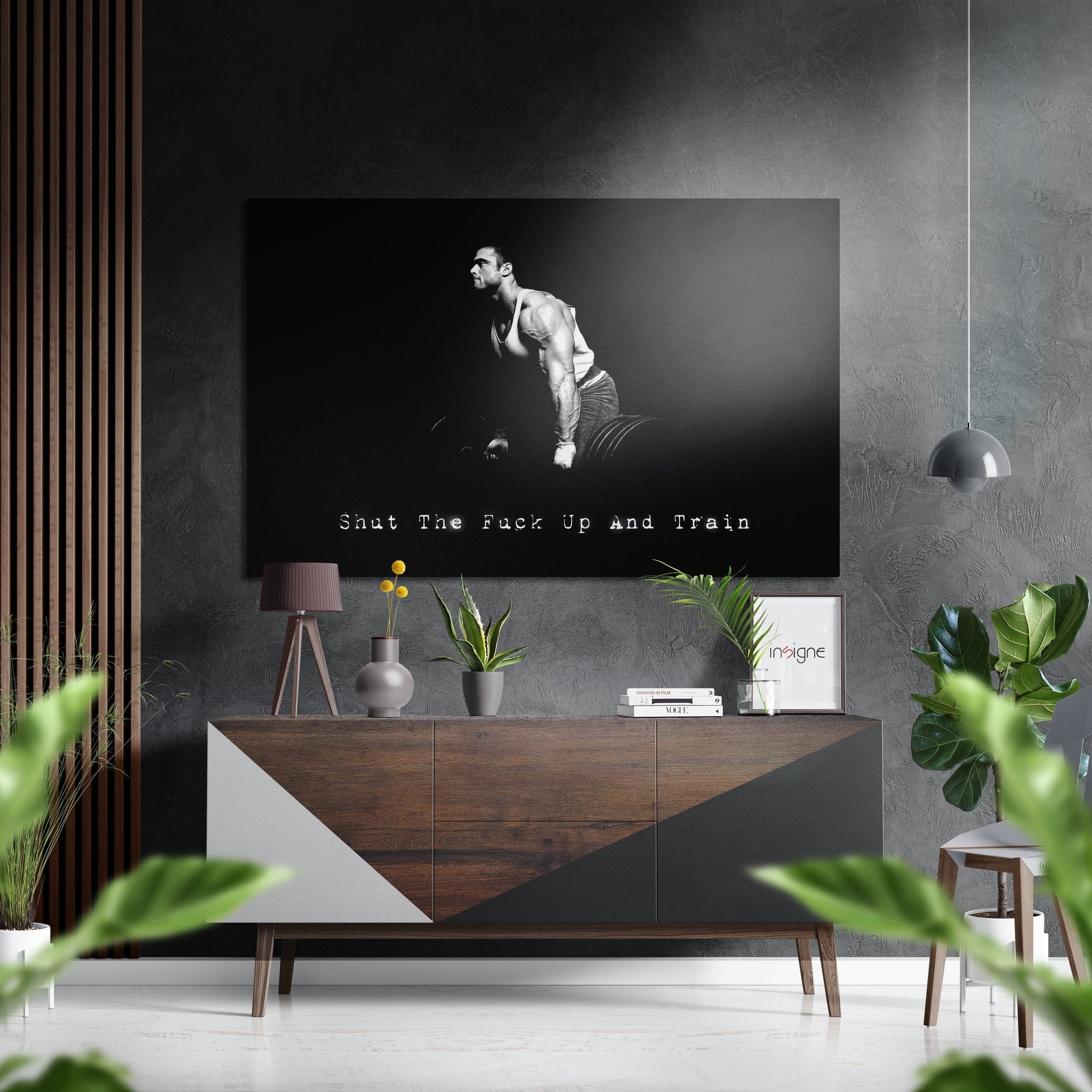 Black and white motivational wall art featuring a muscular man lifting dumbbells with text "Shut The Fuck Up and Train" displayed above a wooden credenza in a modern interior.