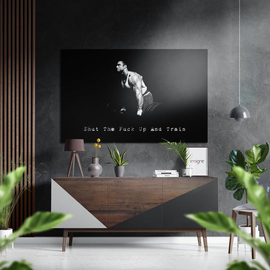 Black and white motivational wall art featuring a muscular man lifting dumbbells with text "Shut The Fuck Up and Train" displayed above a wooden credenza in a modern interior.