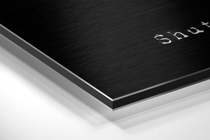 Close-up angled view of layered Dibond wall art with brushed black aluminum top surface and white base layer, showing "Snowy" text.
