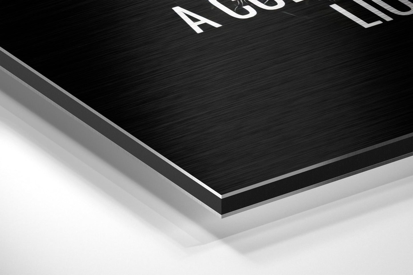 Close-up angled view of layered Dibond wall art showing brushed black surface with white text and silver aluminum edge detail against white background.