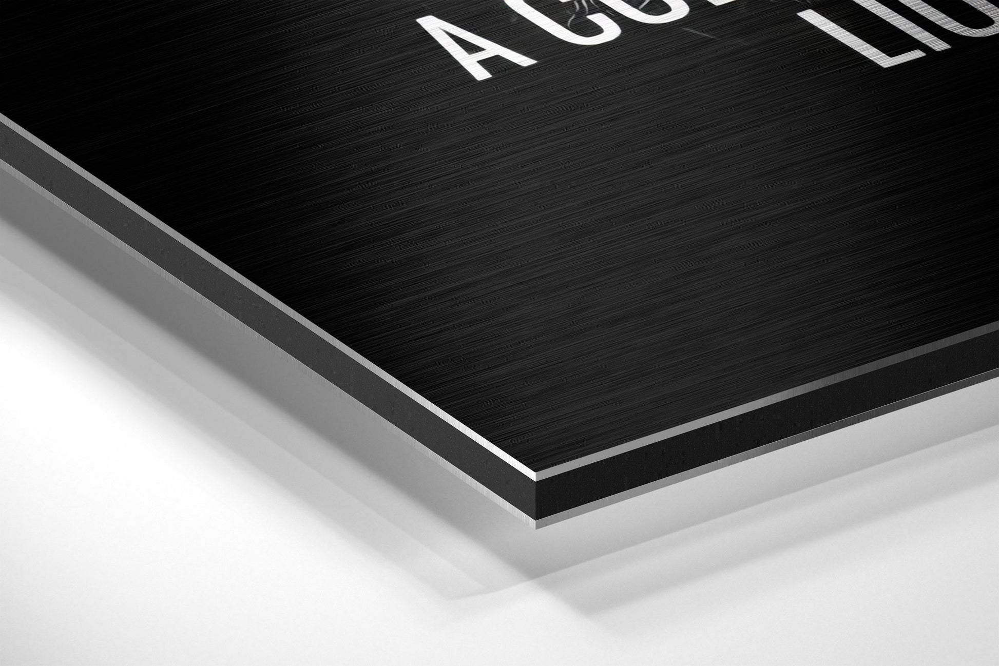 Close-up angled view of layered Dibond wall art showing brushed black surface with white text and silver aluminum edge detail against white background.