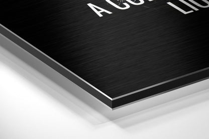 Close-up angled view of layered Dibond wall art showing brushed black surface with white text and silver aluminum edge detail against white background.