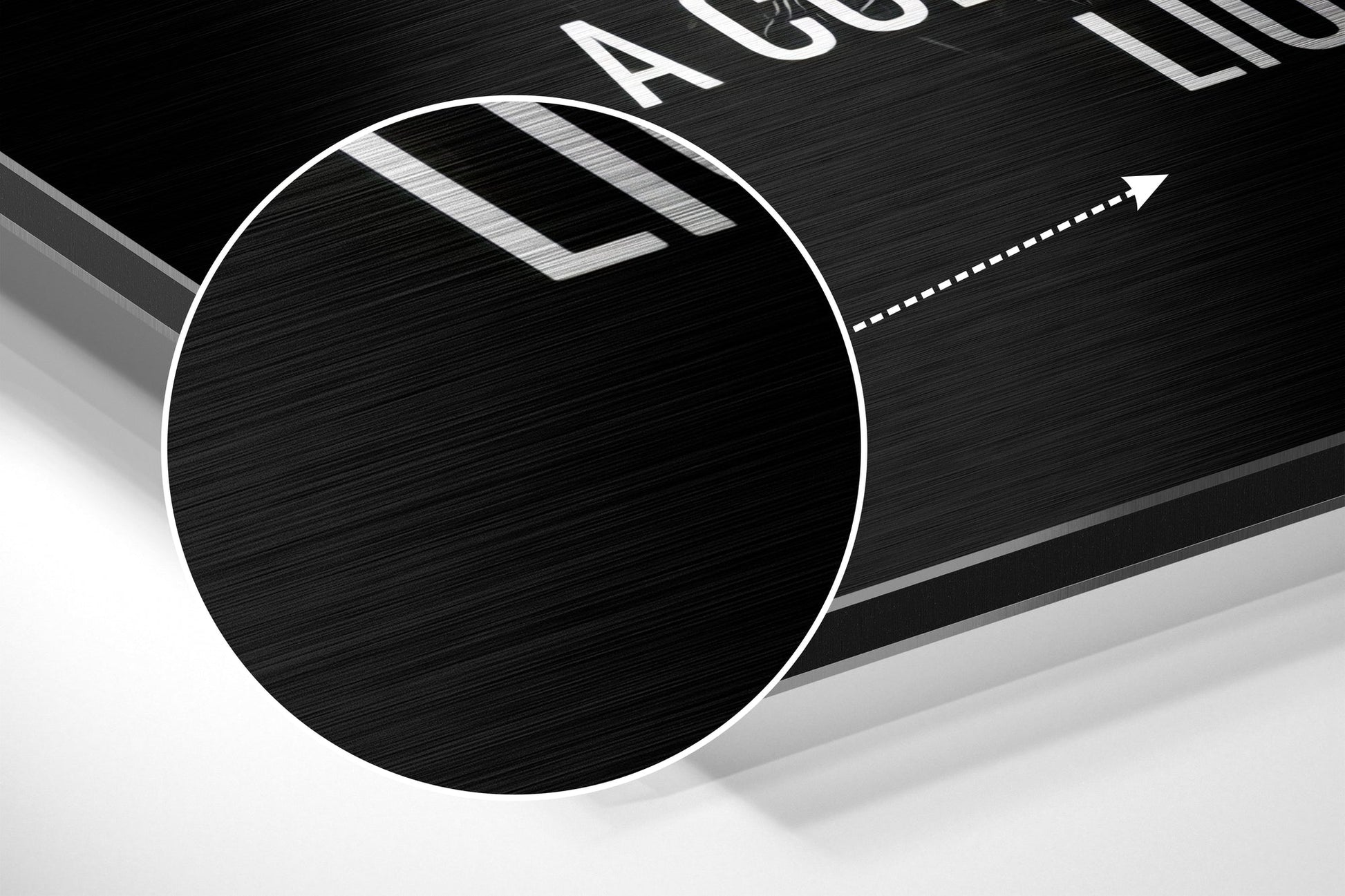 Close-up angled view of circular brushed aluminum Dibond wall art with white border and directional arrow graphic on black textured surface.
