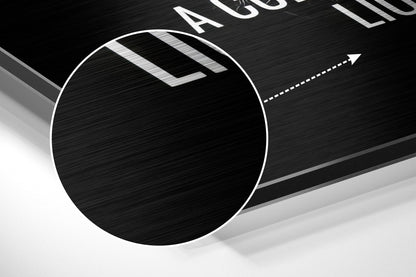 Close-up angled view of circular brushed aluminum Dibond wall art with white border and directional arrow graphic on black textured surface.
