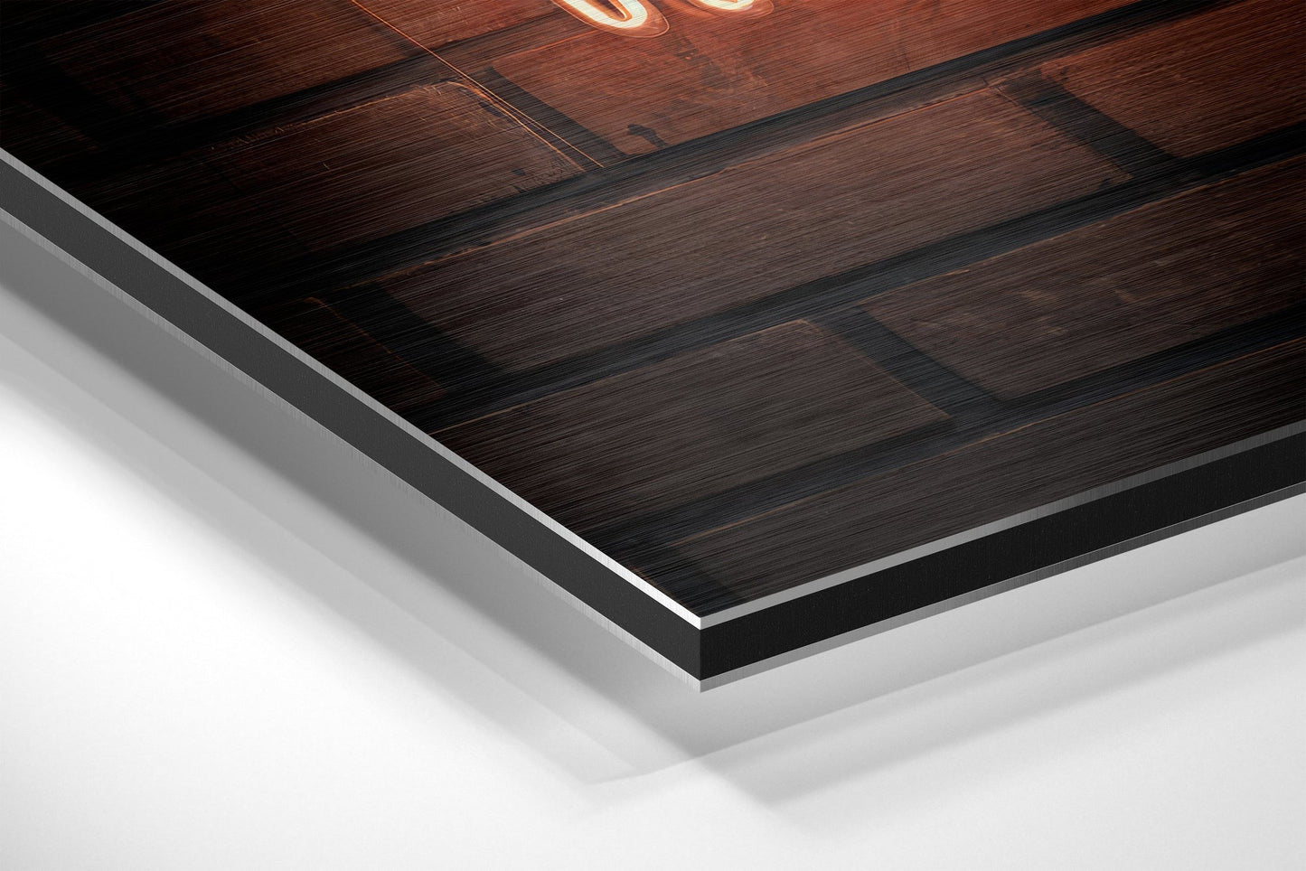 Close-up angled view of brushed aluminum Dibond wall art with dark wood grain texture and neon orange lettering visible on the surface.