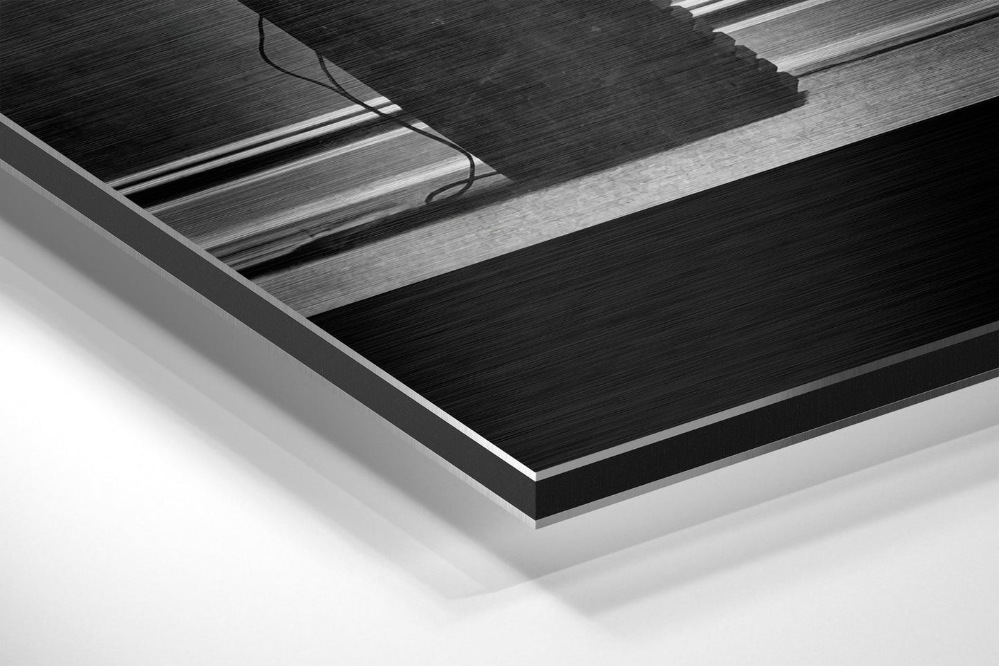 Close-up angled view of brushed aluminum Dibond wall art with layered black and silver metallic panels and visible power cable.