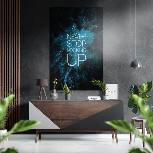 Modern interior scene featuring teal starfield canvas art with "Never Stop Looking Up" text displayed above wooden dresser with potted plants and pendant lighting.