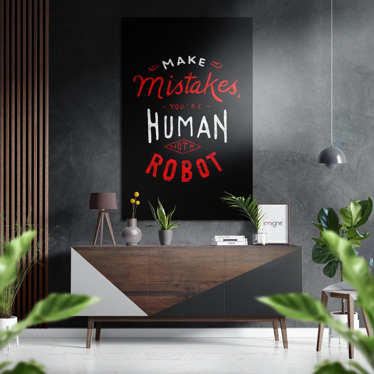 Modern living room interior with black brushed aluminium wall art displaying red and white typography quote above wooden sideboard with plants and accessories.