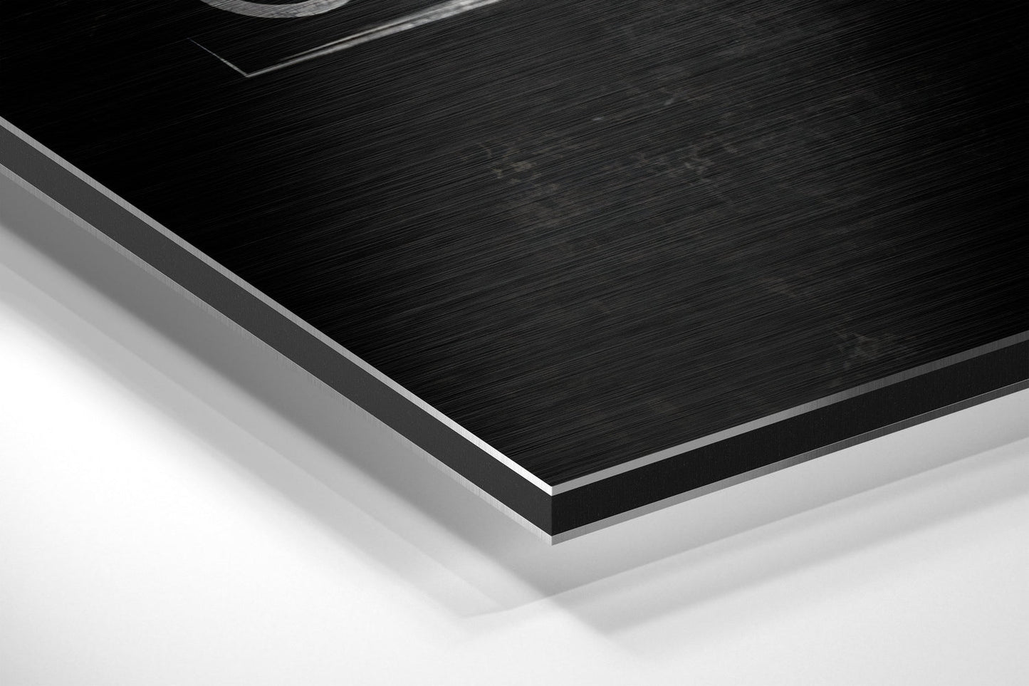 Close-up angled view of brushed black aluminium Dibond panel with silver beveled edge against white background.