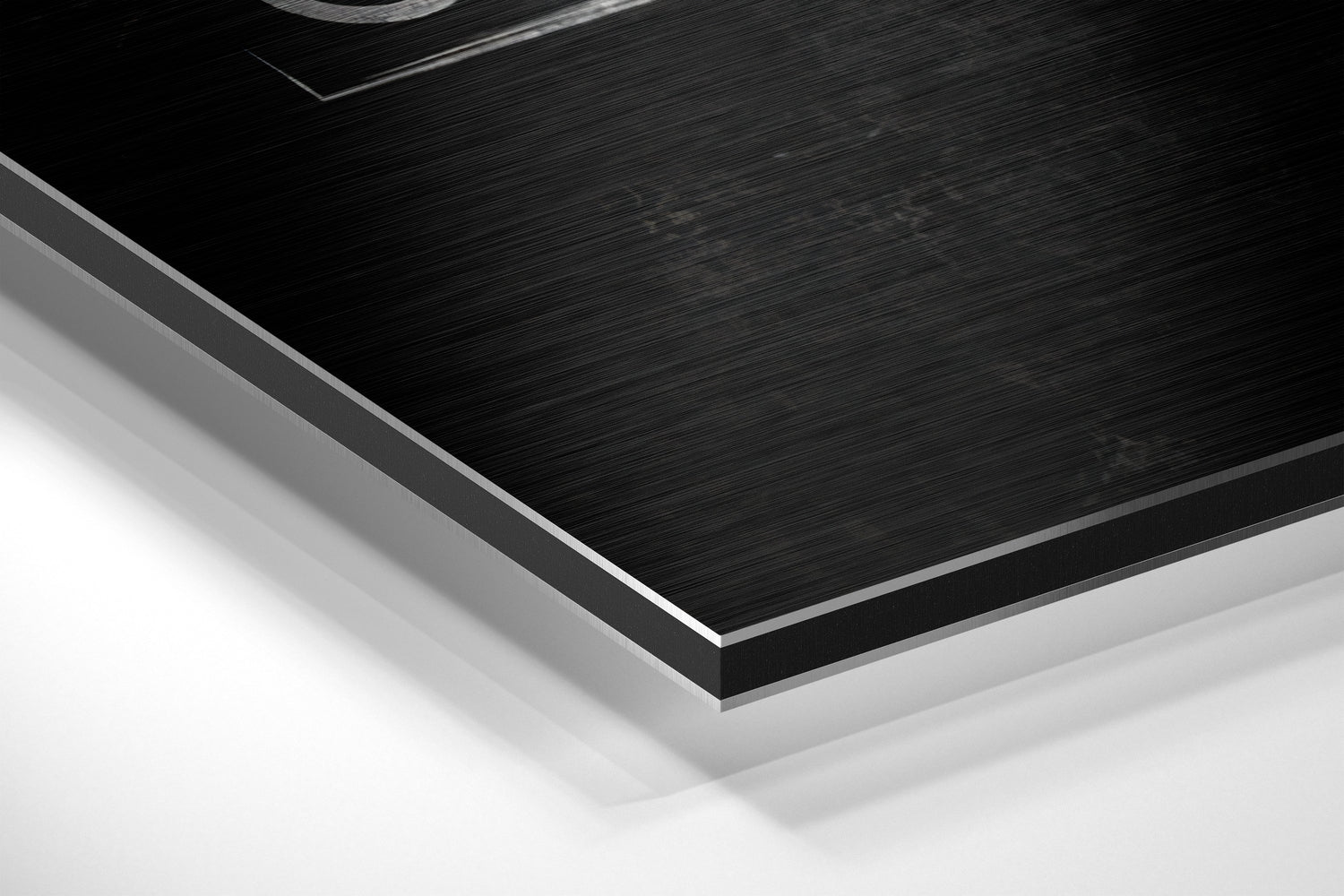 Close-up angled view of brushed black aluminium Dibond panel with silver beveled edge against white background.