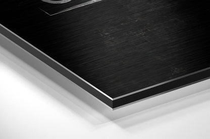 Close-up angled view of brushed black aluminium Dibond panel with silver beveled edge against white background.