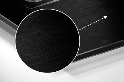 Angled closeup of brushed black aluminum circular wall art with white border outline and directional arrow detail.