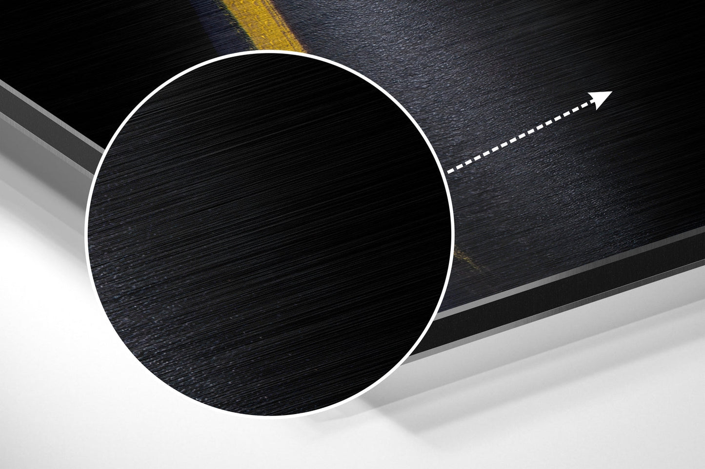 Overhead view of brushed black aluminium circular wall art with white border on asphalt road with yellow line and directional arrow.