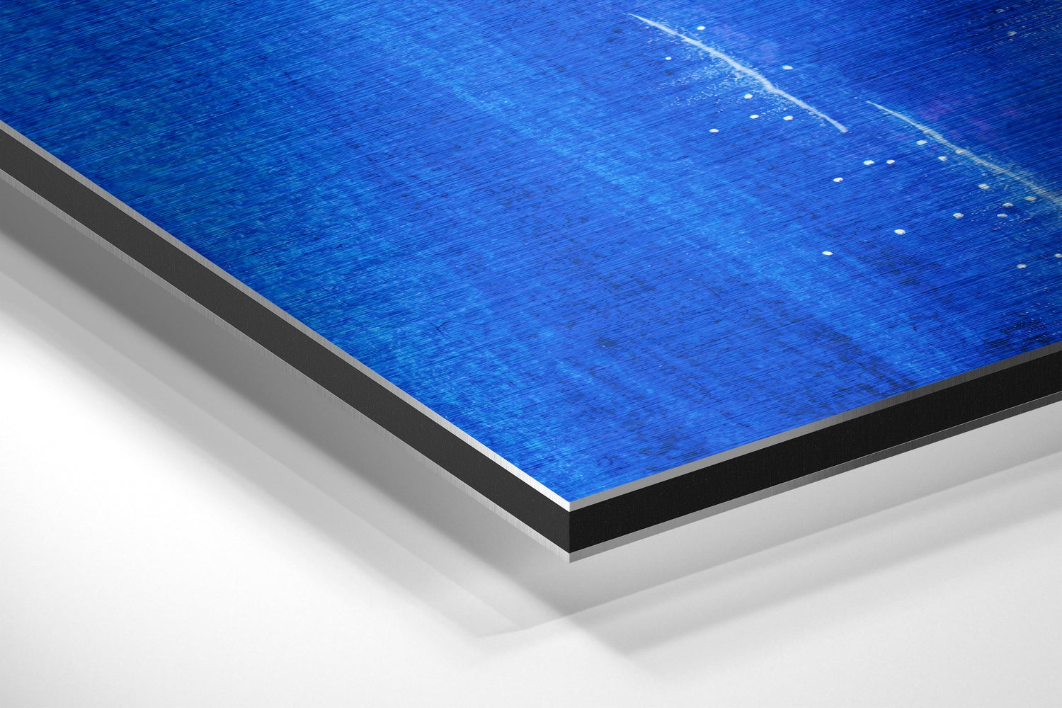 Close-up angled view of brushed aluminum Dibond panel with blue metallic surface and layered edge detail against white background.