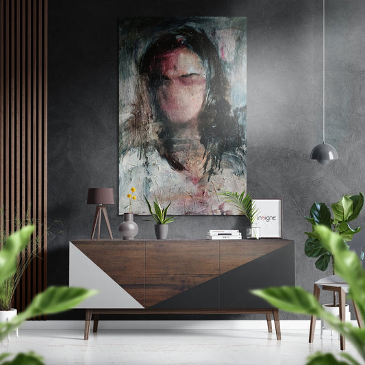 Modern interior with abstract portrait artwork mounted above wooden dresser with white geometric panel, styled with lamp, plants, and decorative objects.