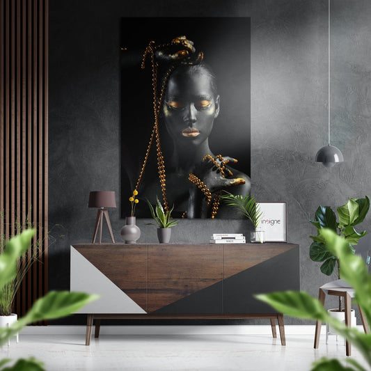 Black woman with golden beads and closed eyes displayed on dark wall art above wooden console in modern interior setting.