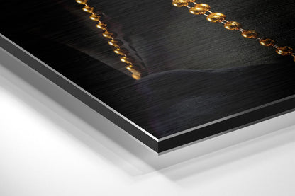 Close-up angled view of black brushed aluminum Dibond panel with gold chain detail along top edges against white background.