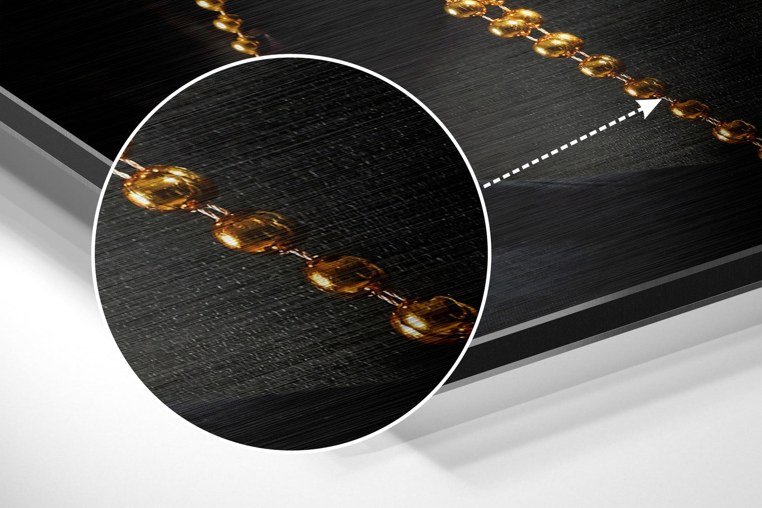 Close-up detail of gold chain links on textured black brushed aluminium surface with magnified circular inset showing chain pattern.