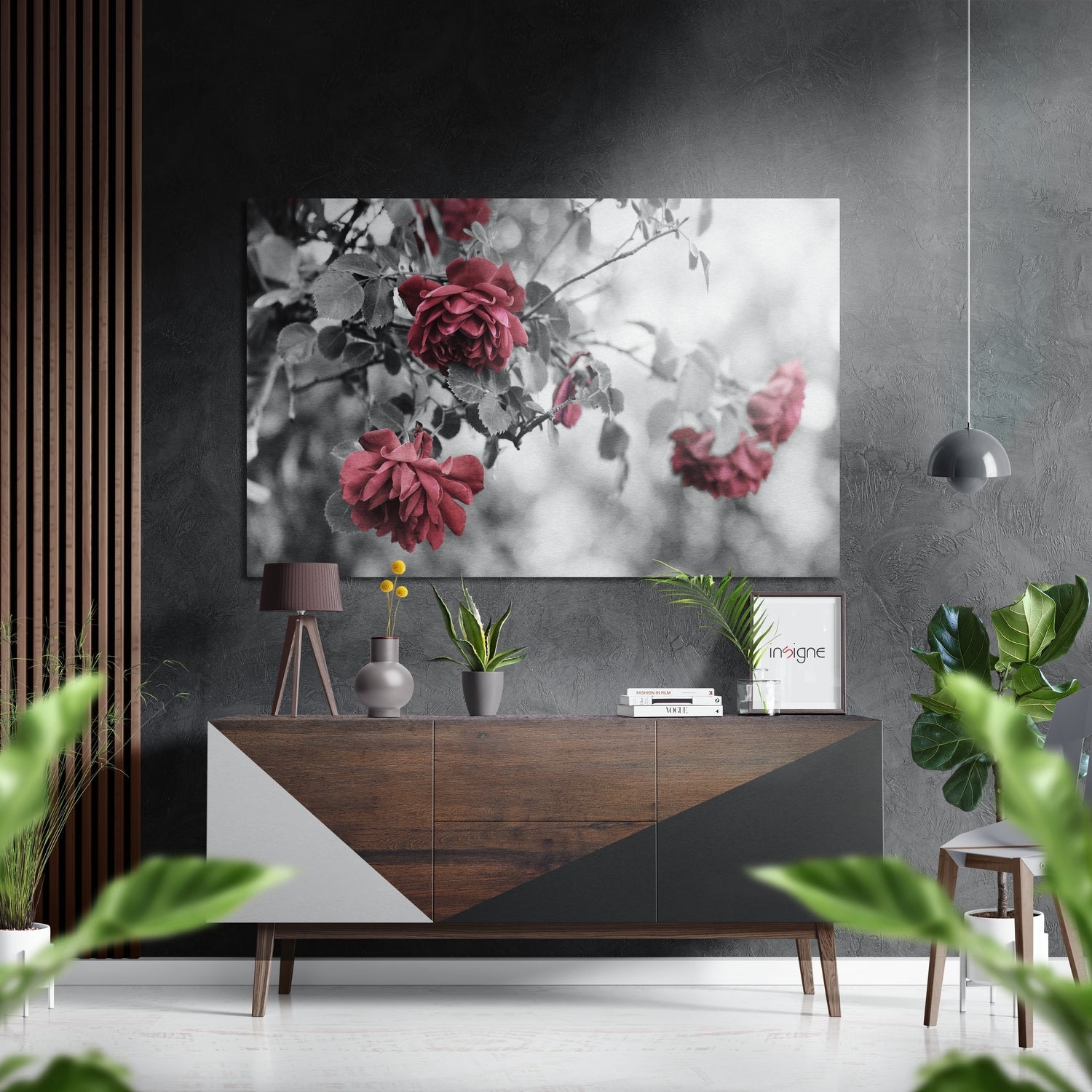 Red roses in black and white selective color displayed on gray wall above wooden console table in modern interior setting.