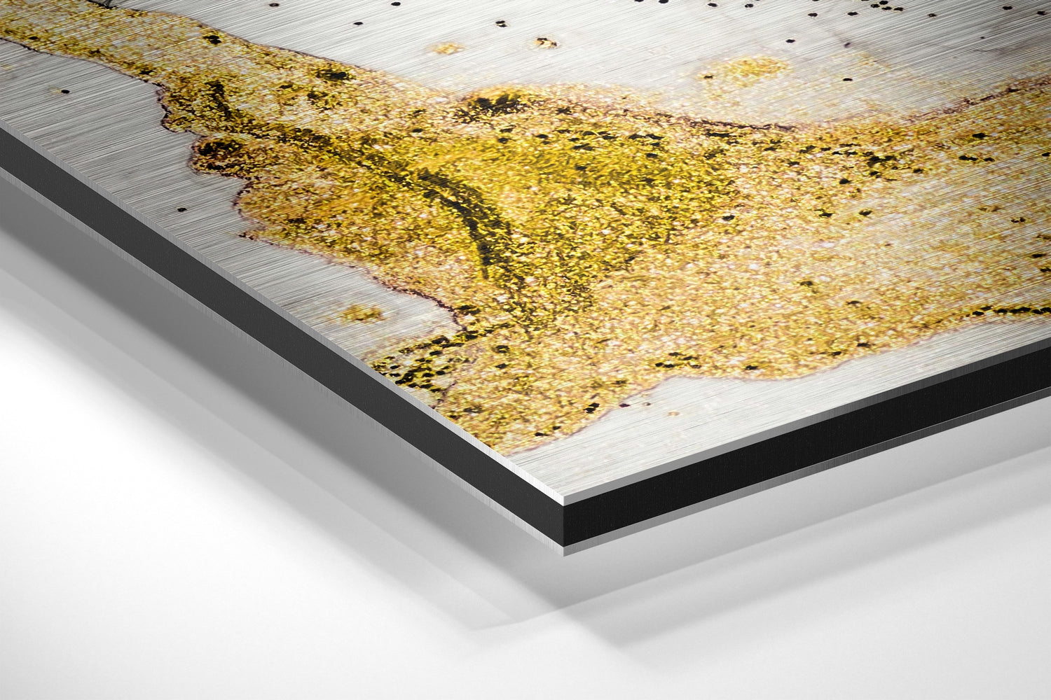 Close-up angled view of layered Dibond panel showing brushed aluminum surface with gold glitter abstract design and black border edge.