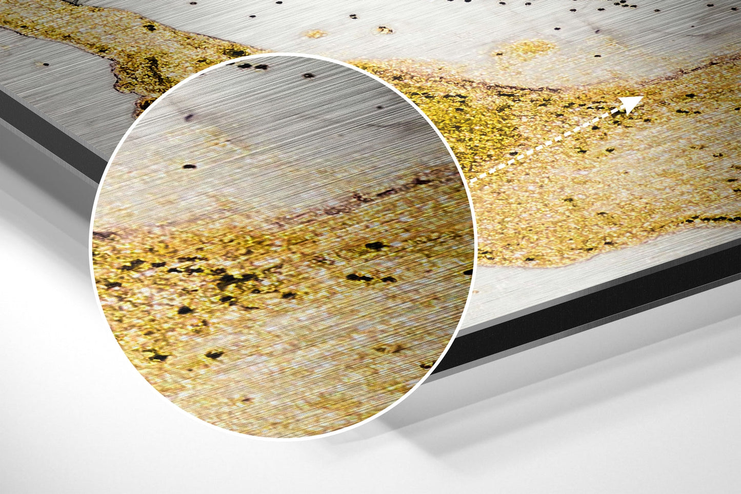 Close-up detail of golden marble brushed aluminum surface with black speckles and wood grain texture, magnified circular view.
