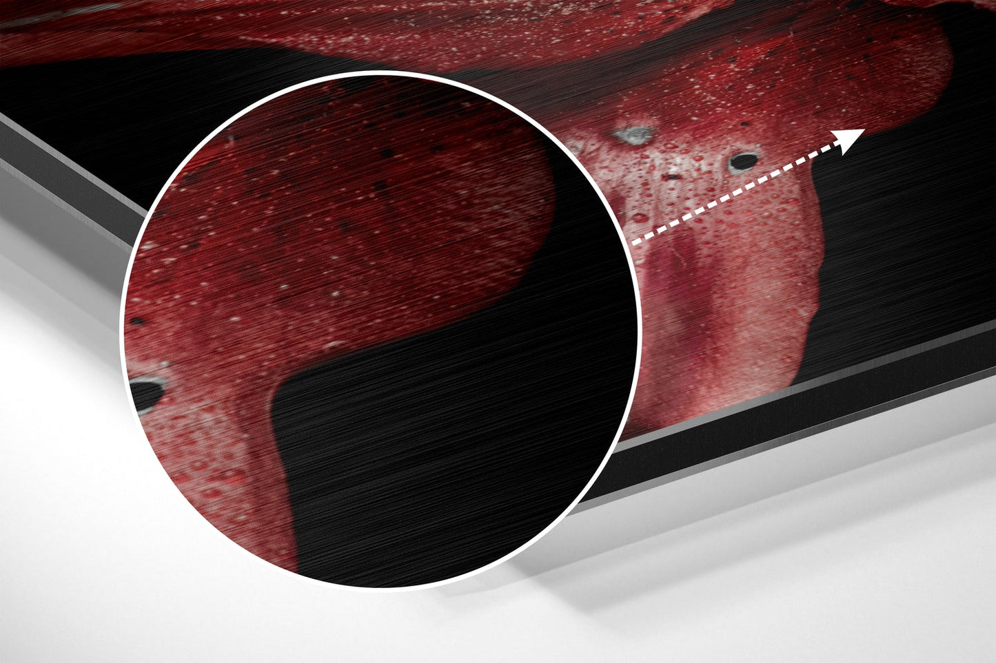 Close-up detail of red brushed aluminium surface with circular magnified section showing texture and dark speckles.