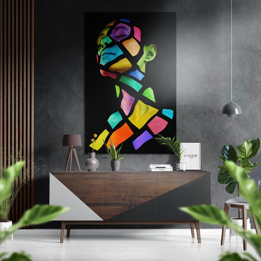 Colorful geometric pop art portrait with vibrant neon sections mounted on dark wall above wooden dresser in modern interior setting.