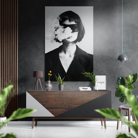 Black and white portrait of woman wearing sunglasses and exhaling smoke, displayed as wall art above wooden console in modern interior setting.
