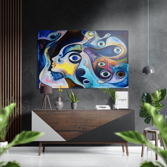 Colorful abstract aluminum wall art featuring stylized faces and multiple eyes in blue, yellow, and orange tones displayed above a wooden dresser in a modern interior.