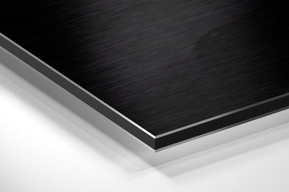 Close-up angled view of layered Dibond panel showing black brushed aluminum surface with gray and white backing layers.