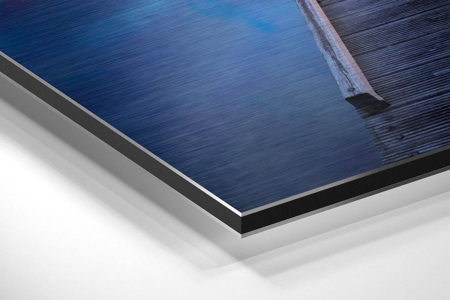 Close-up angled view of layered Dibond wall art showing brushed blue and grey metallic surface with white backing and black edge detail.