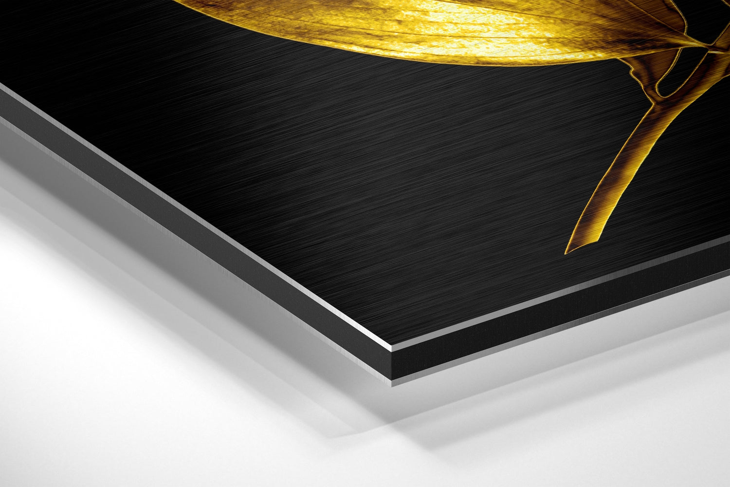 Angled perspective view of layered Dibond panel showing black brushed aluminum surface with gold leaf design and silver edge detail.