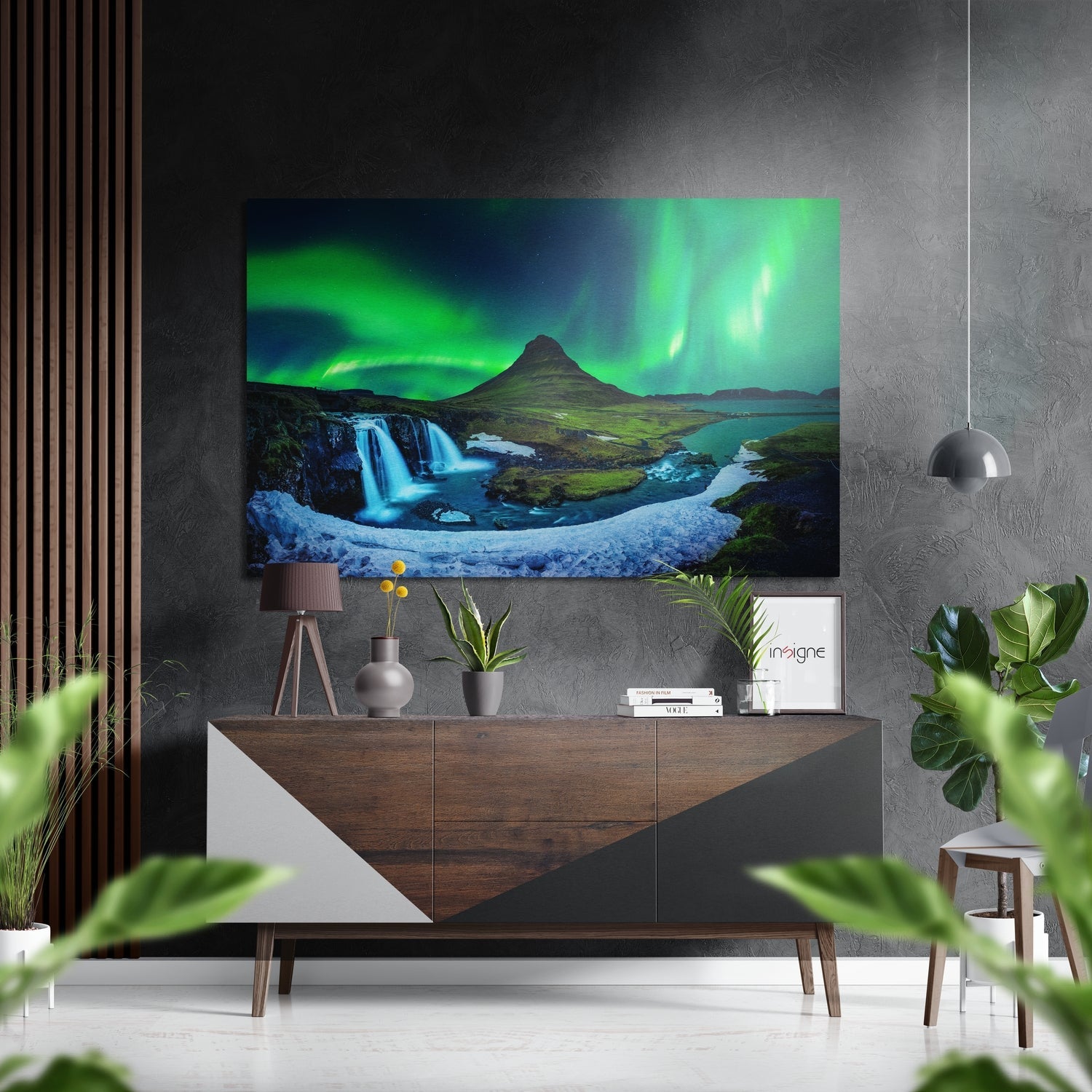 Northern lights landscape photograph mounted above wooden dresser in modern interior setting with plants and pendant light.