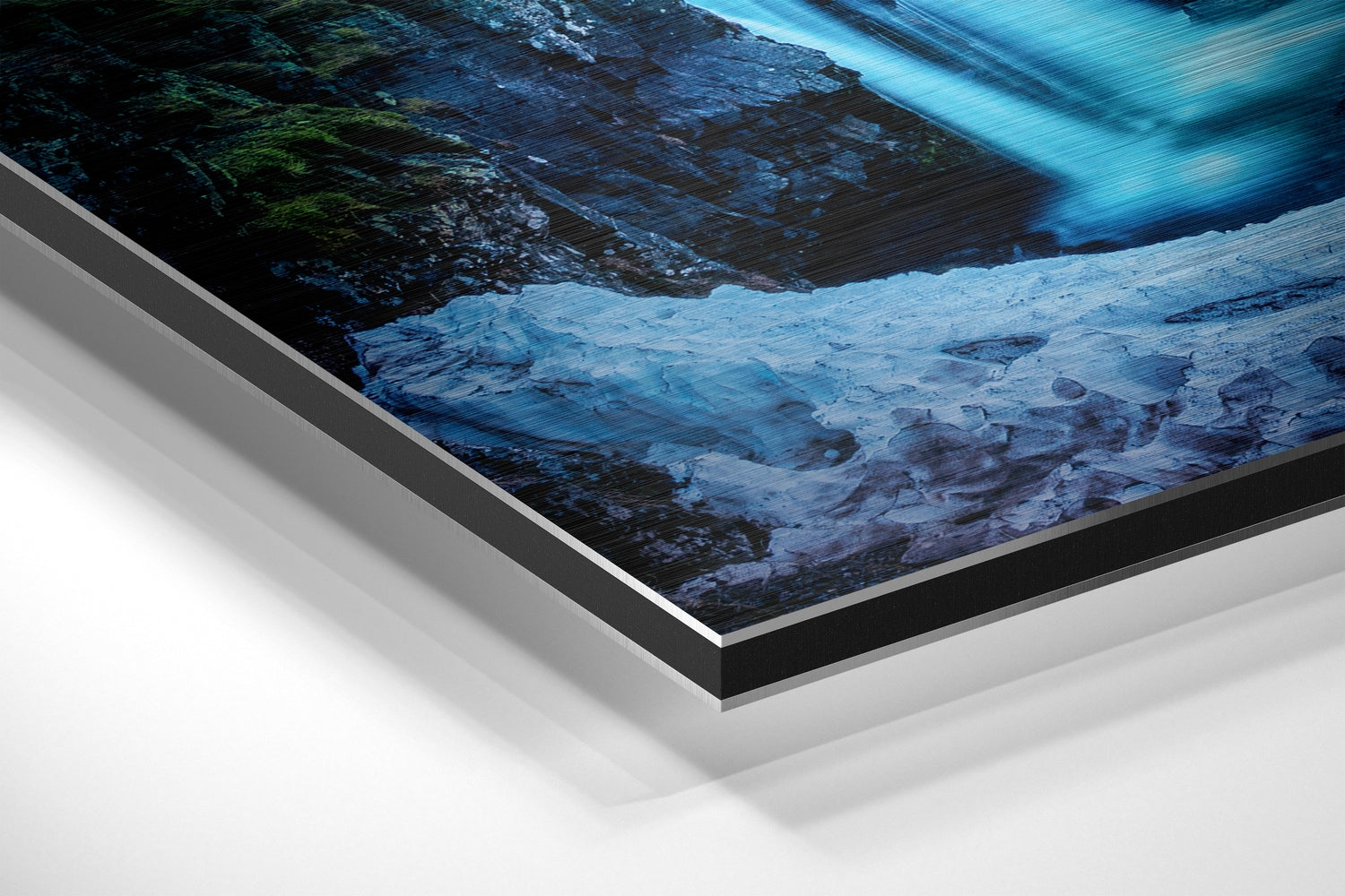 Angled view of brushed aluminium Dibond wall art displaying a glacier landscape with blue ice, dark rock, and flowing water detail.