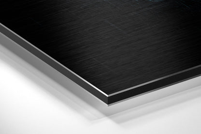 Close-up angled view of layered Dibond panel showing brushed black aluminum surface with gray and white backing layers.