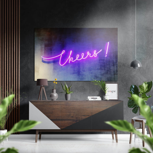 Pink and purple neon "Cheers!" script sign displayed on textured gray wall above wooden console table in modern interior setting.