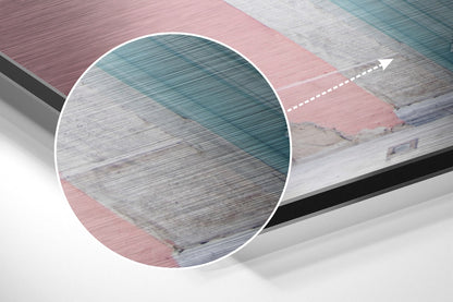 Close-up detail of brushed aluminium wall art showing layered pink, grey, and teal horizontal texture with circular magnified section and directional arrow.