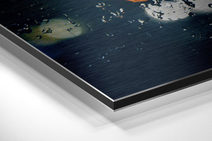 Close-up angled view of layered Dibond wall art showing brushed aluminum edges and white backing with dark blue water scene featuring scattered light reflections.