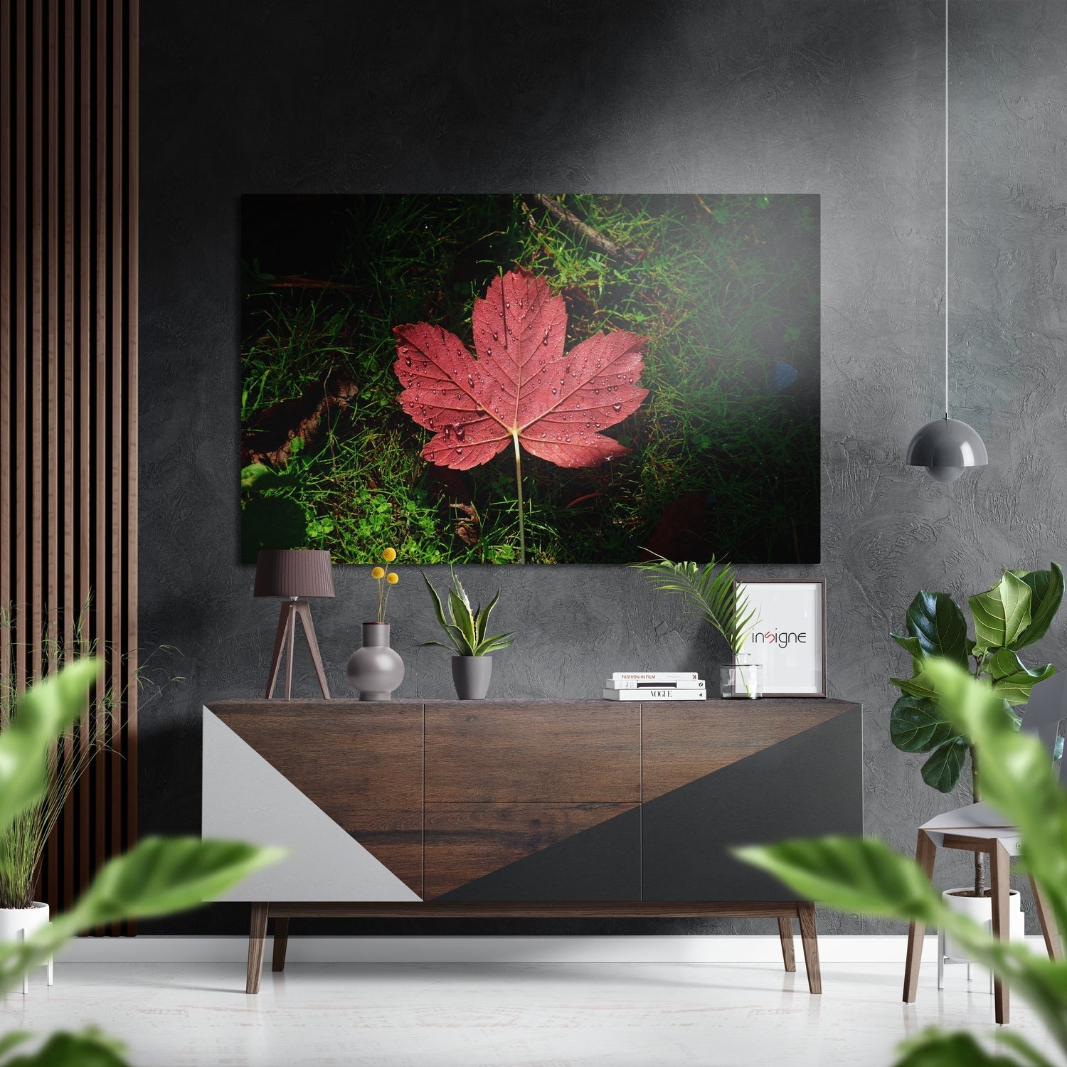 Red autumn leaf with water droplets displayed above a wooden console table in a modern interior setting.