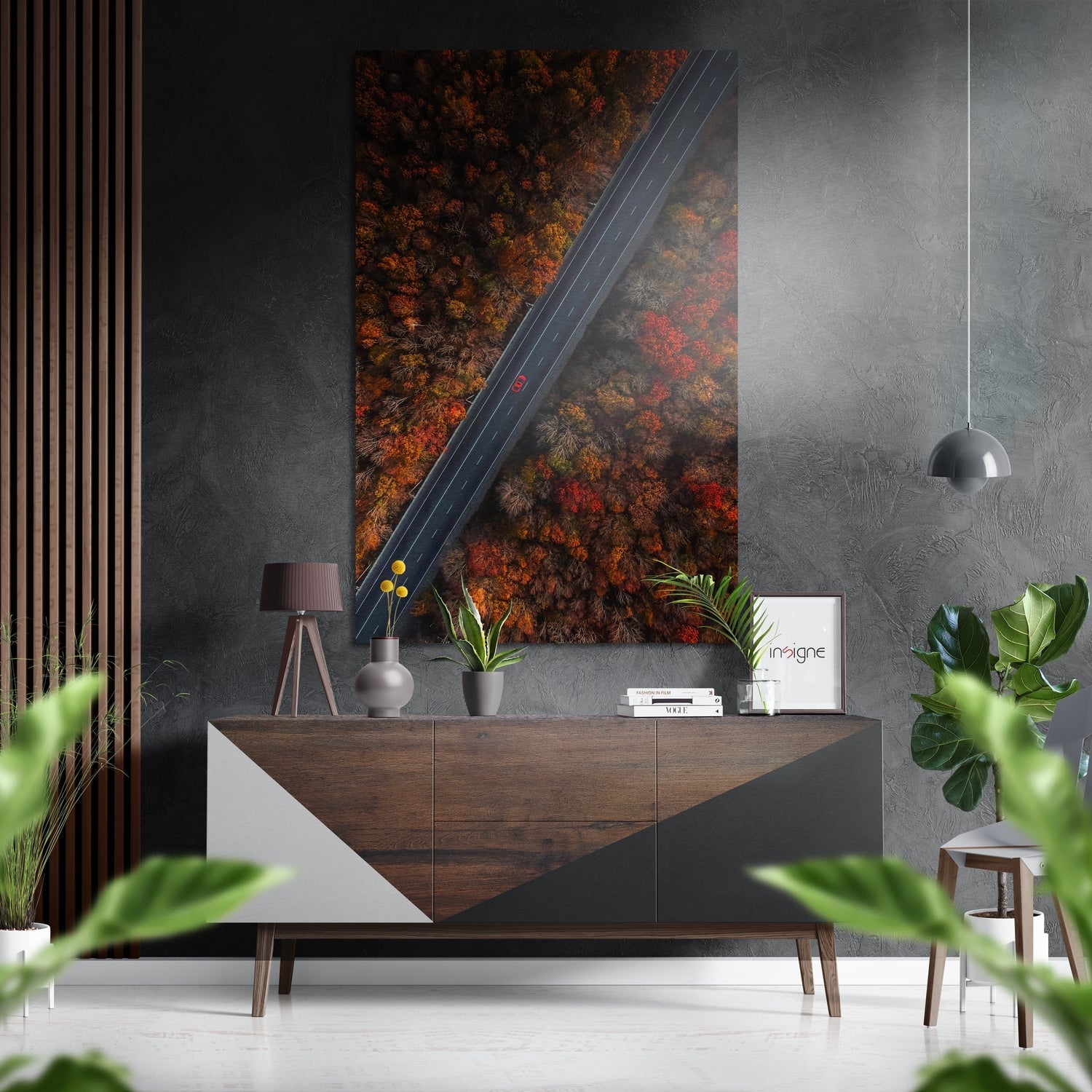 Aerial view of autumn forest with red and orange foliage bisected by a dark asphalt road, displayed as wall art above a wooden dresser.