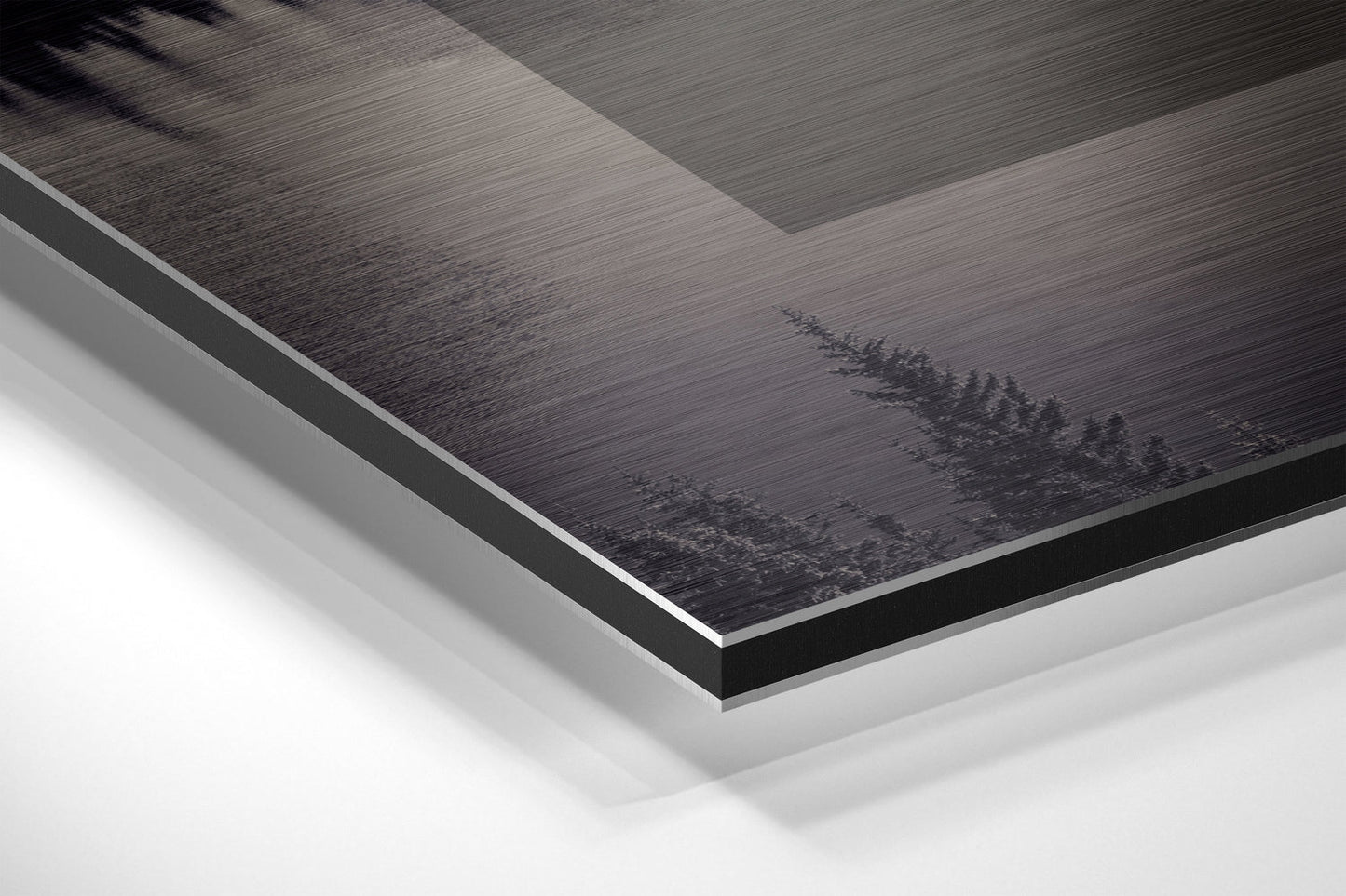 Close-up angled view of layered Dibond panel showing brushed aluminum surface with dark forest treeline design and white backing board edge.