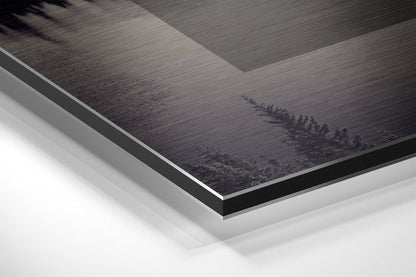 Close-up angled view of layered Dibond panel showing brushed aluminum surface with dark forest treeline design and white backing board edge.
