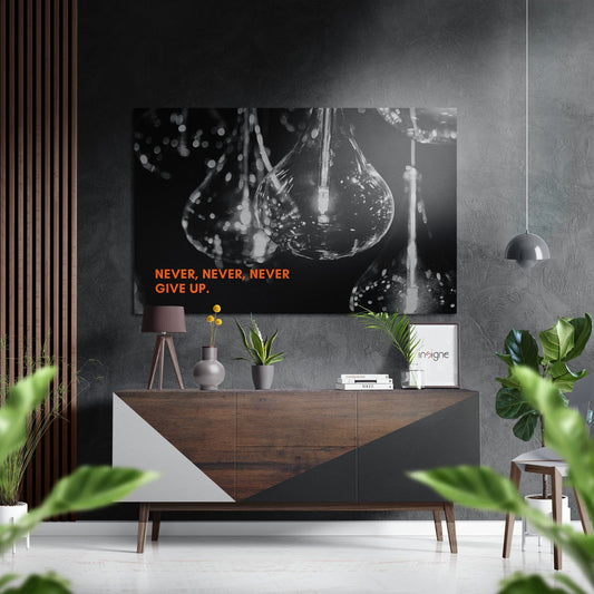 Black and white photograph of illuminated light bulbs with orange text "NEVER, NEVER, NEVER GIVE UP" displayed above wooden console in modern interior setting.