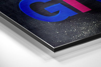 Angled closeup of brushed aluminium Dibond wall art showing layered construction with blue graphic and pink accent on textured black surface.