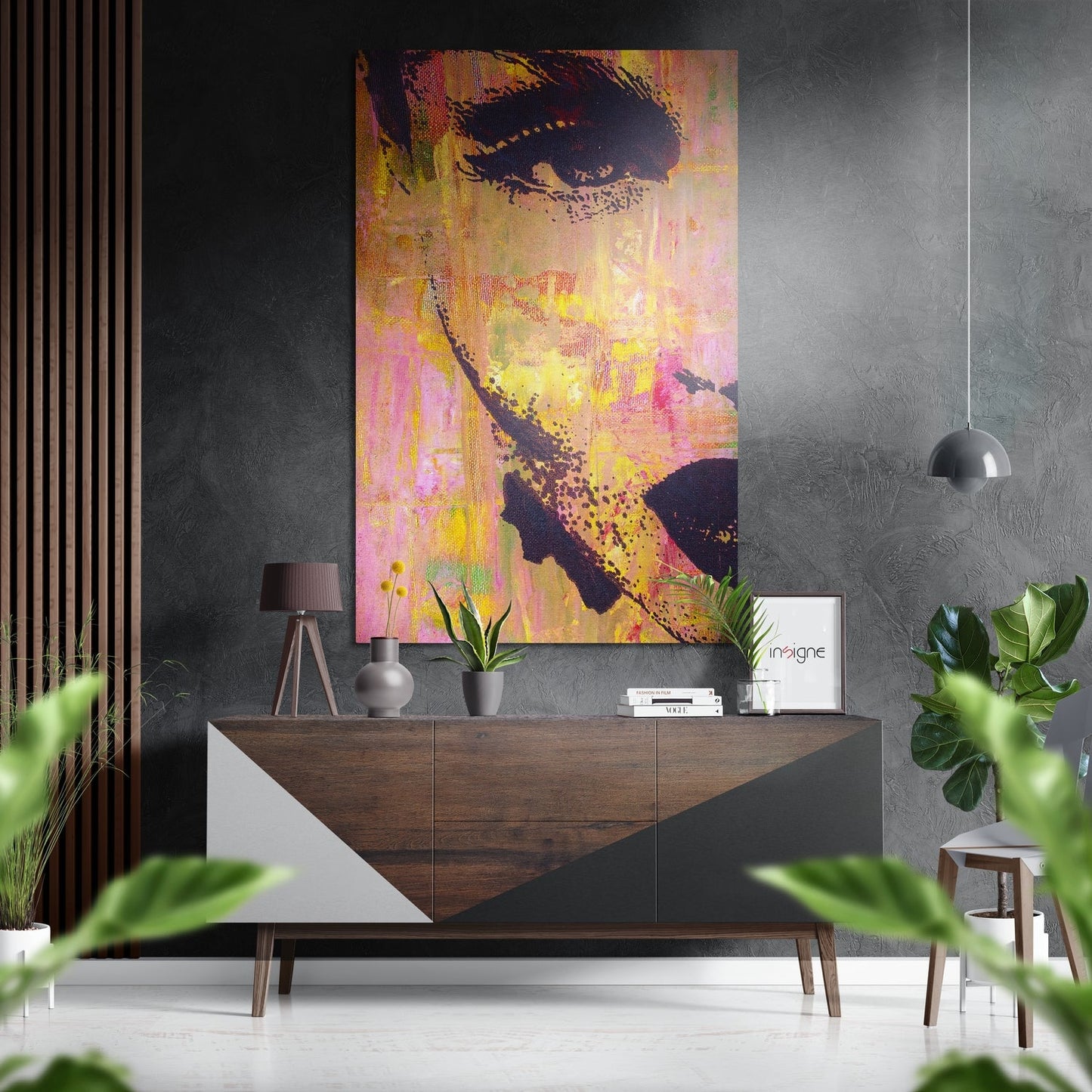 Colorful pop art portrait of a woman's face in yellow, pink, and black displayed on a dark textured wall above a wooden sideboard in a modern interior.