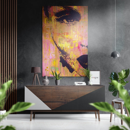 Colorful pop art portrait of a woman's face in yellow, pink, and black displayed on a dark textured wall above a wooden sideboard in a modern interior.